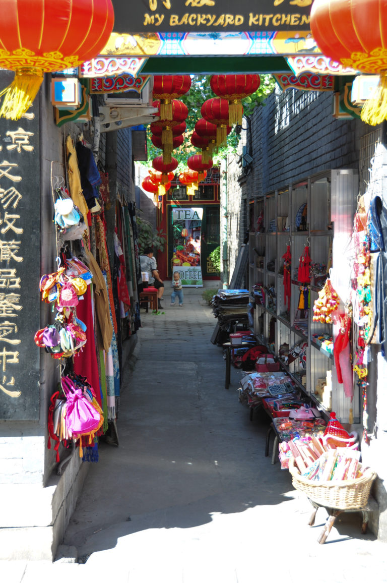 Narrow souvenir and tea-shopping lane lined with colorful goods in a Beijing hutong district.