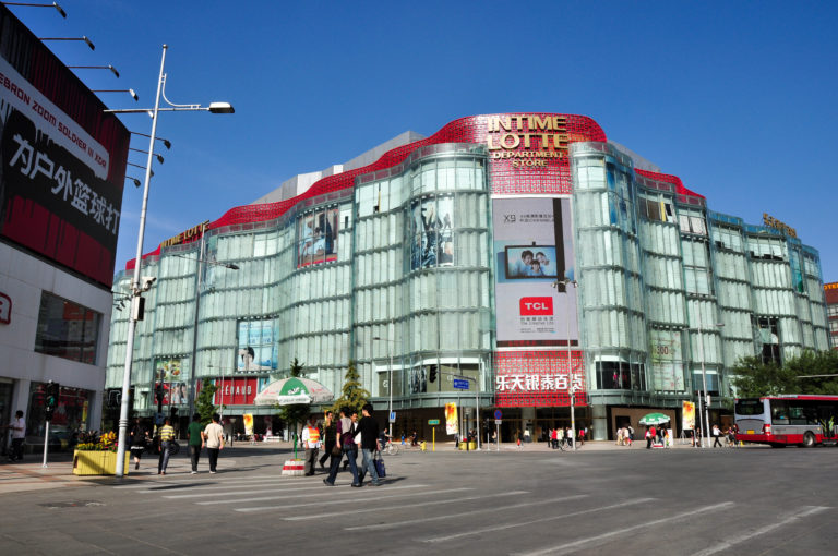 Curved glass-fronted Intime Lotte department store with INTIME LOTTE and TCL signs at a Beijing intersection.