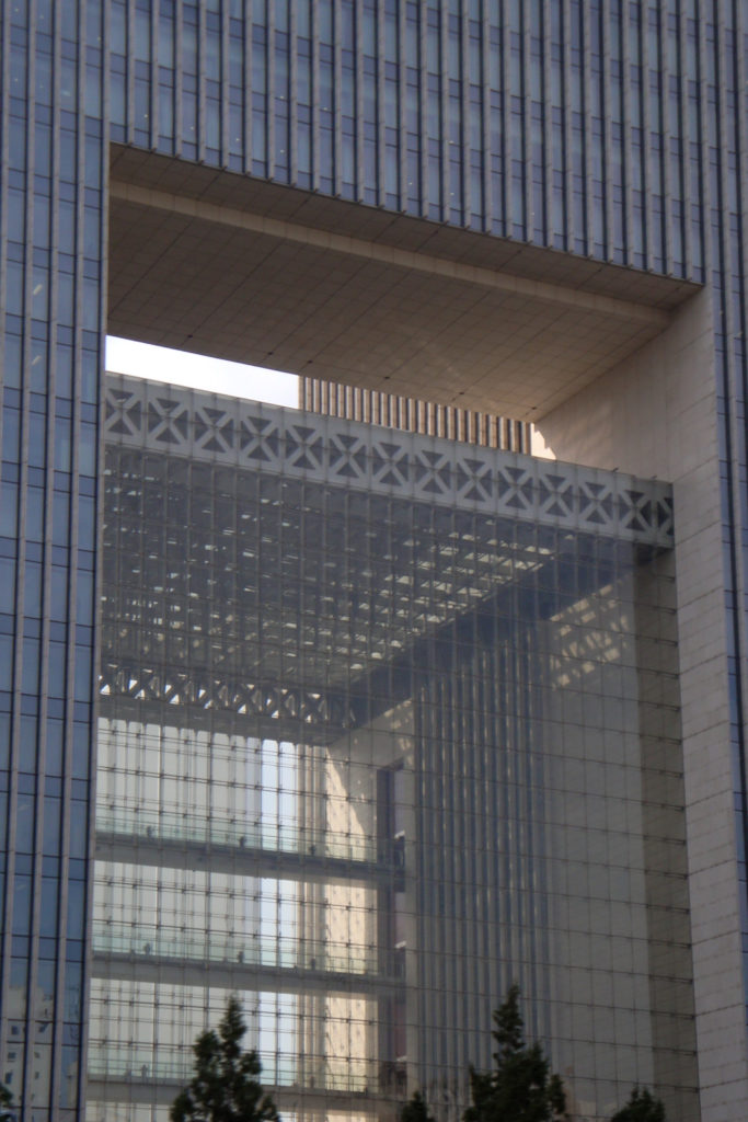 Close view of a several-story rectangular opening in a modern Beijing office building, revealing diagonal steel trusses behind glass within a ribbed facade.