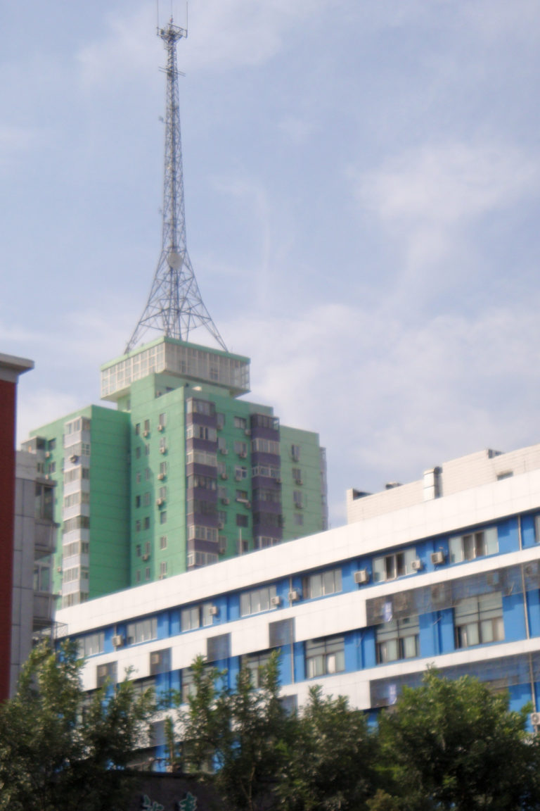 Green and purple apartment tower in central Beijing with a large lattice antenna structure on the roof behind lower commercial buildings.