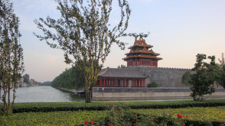 Corner tower of the Forbidden City beside the calm palace moat and gray stone walls in Beijing.