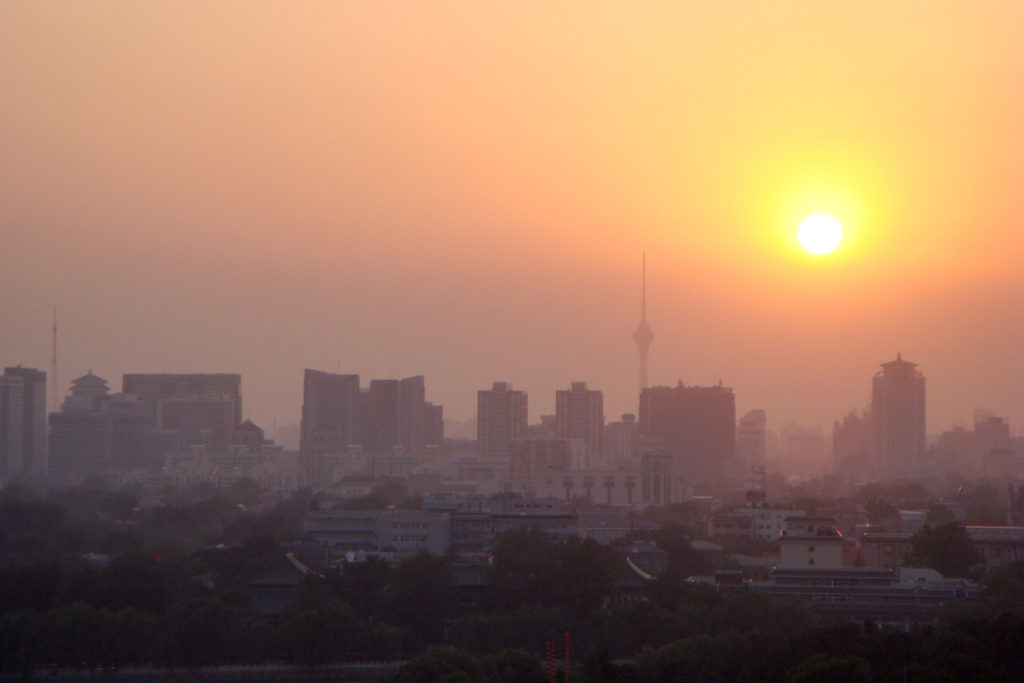 Orange sunset over Beijing skyline with a communications tower and high-rise buildings seen through haze.