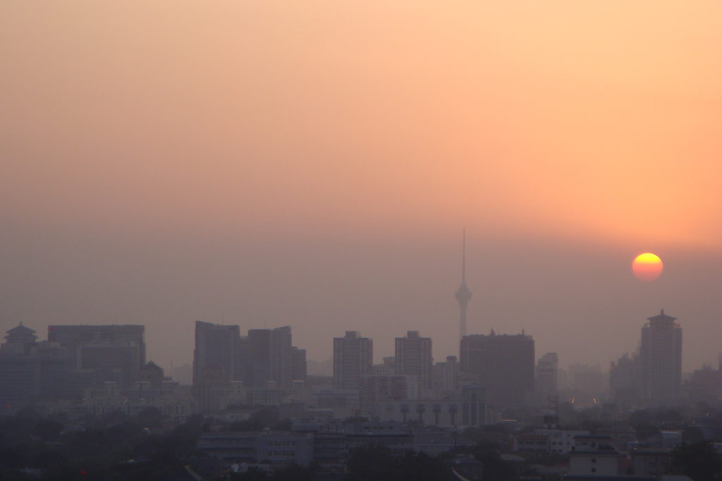 Hazy sunset over central Beijing with the slender Central Radio and Television Tower silhouetted against an orange sky.