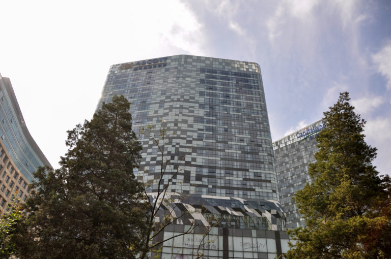 Modern Beijing office tower with a rounded rectangular form and irregular checkerboard facade of gray, white, and blue glass panels.