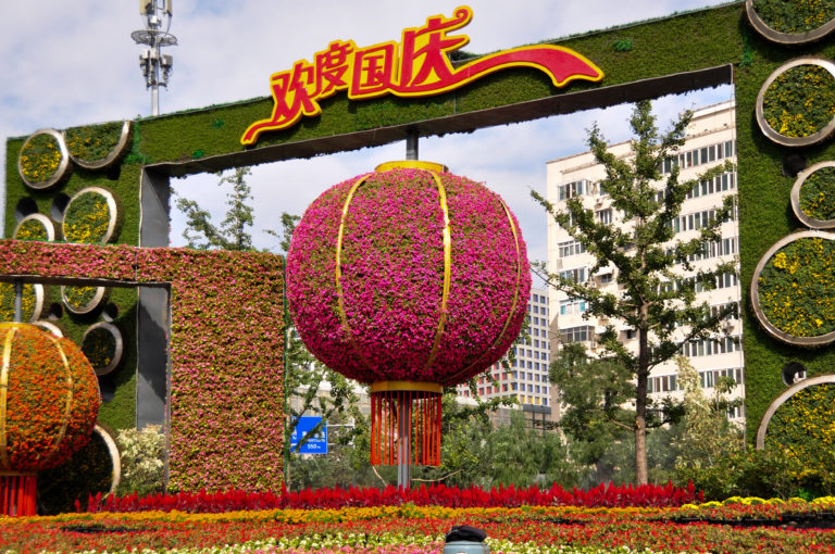 Giant magenta flower-covered lantern made of living plants beneath a 欢度国庆 National Day sign in Beijing.
