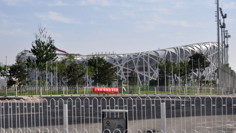 Beijing National Stadium, the Bird’s Nest, seen across a wide controlled roadway with its interwoven steel lattice frame clearly visible.