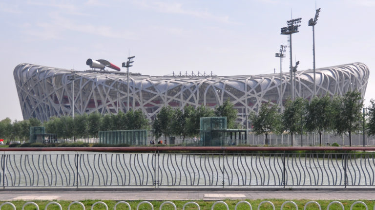Wide exterior view of Beijing National Stadium, the Bird’s Nest, showing its irregular interwoven steel lattice and oval stadium bowl.