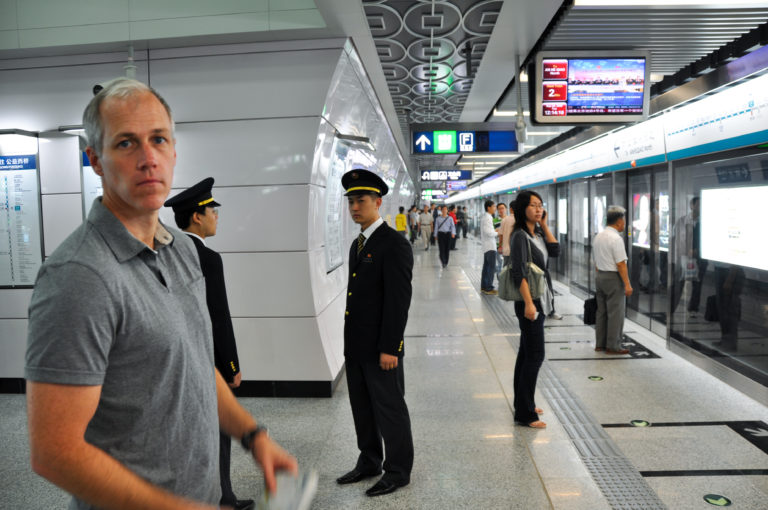 Traveler standing on a Beijing subway platform with two uniformed staff near full-height platform screen doors.