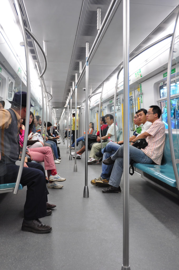 Passengers seated along both sides of a modern Beijing subway carriage with longitudinal benches and central standing space.