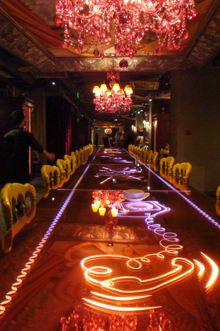 Very long glossy dining table with embedded purple lighting, lined with yellow chairs in a dark Beijing restaurant interior.