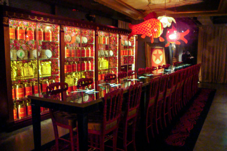 Wide interior view of a Beijing restaurant with a long row of red chairs and glass tables under hanging fish-shaped lanterns and glowing display cabinets.
