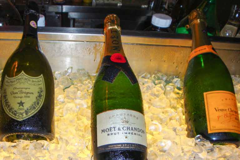 Close-up of Dom Pérignon, Moët & Chandon Brut Impérial, and Veuve Clicquot champagne bottles resting in crushed ice in a bar display.