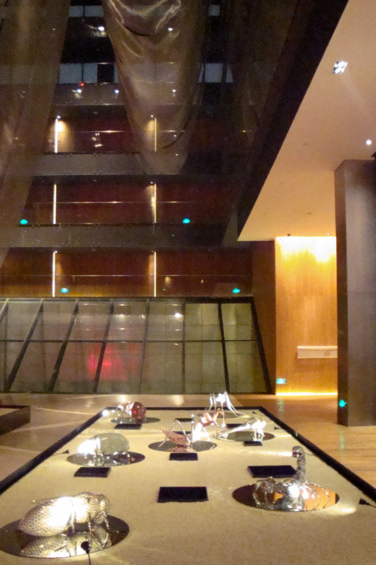 Wide view of a modern Beijing atrium with multiple levels, glass railings, a sloped glass structure, and warm amber wall lighting.