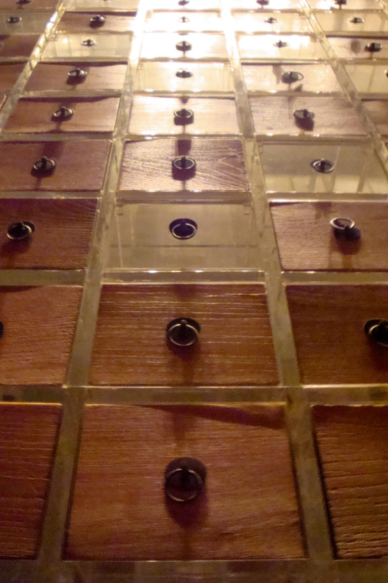 Close-up of a grid of small square wooden drawers with round metal pulls divided by transparent strips.