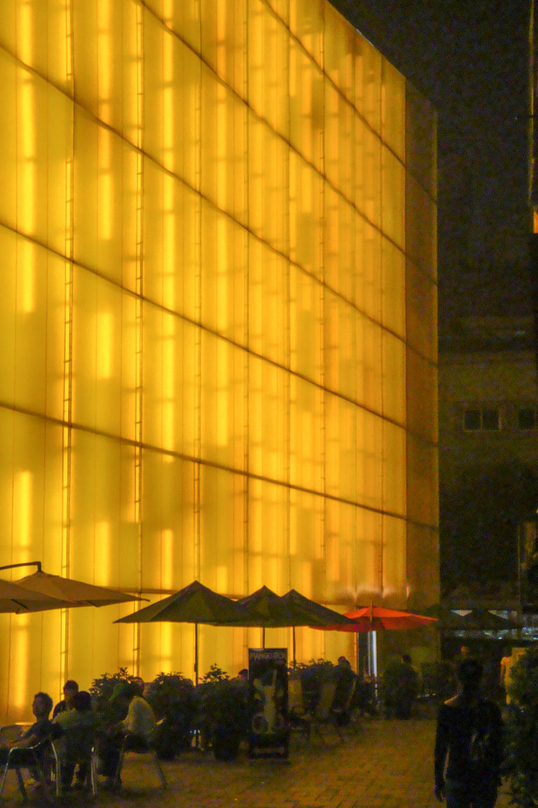 Close view of an amber backlit translucent wall with a rectangular panel grid in a modern Beijing interior, bordered on the right by a dark vertical structure.