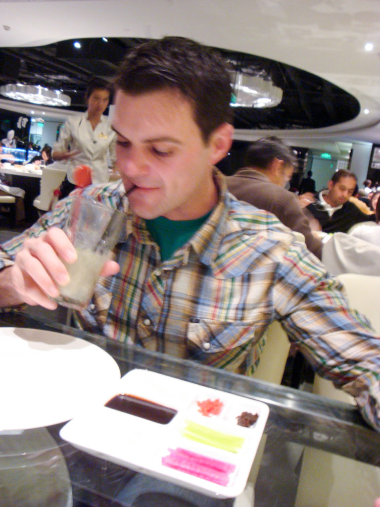 Plaid-shirted diner sipping from a clear glass at a table in a busy contemporary Beijing restaurant.