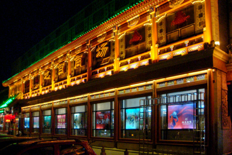 Traditional-style Beijing commercial building at night with illuminated roofline and signage along a commercial street.