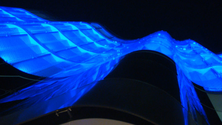 Low-angle nighttime view of an undulating blue-lit translucent tensile canopy above a modern commercial building in Beijing.