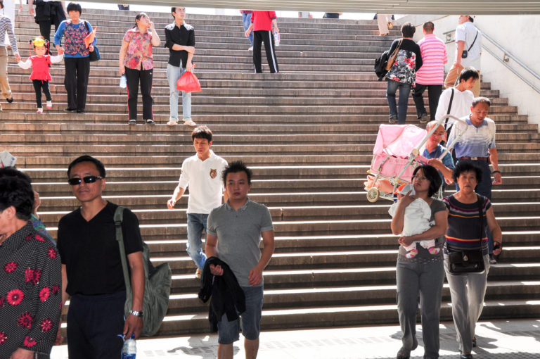 Visitors, including adults and families, walk down a broad stone public stairway.