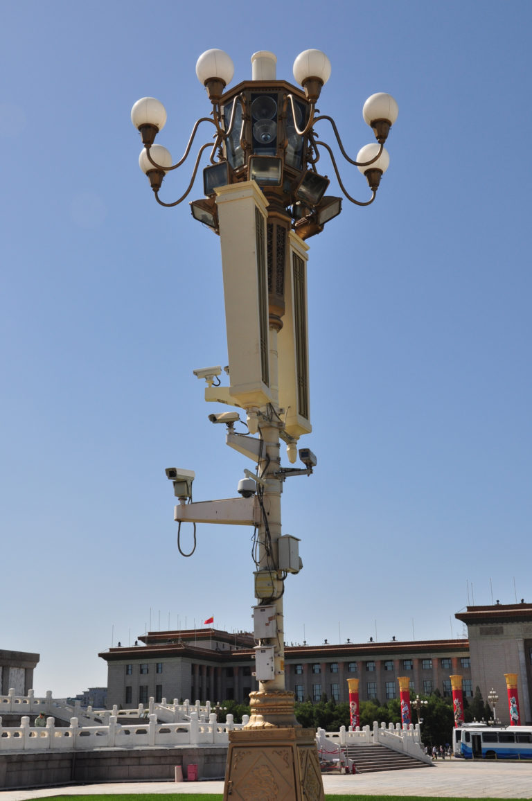 Multiple CCTV cameras and communications devices mounted high on a tall pole against a blue sky.