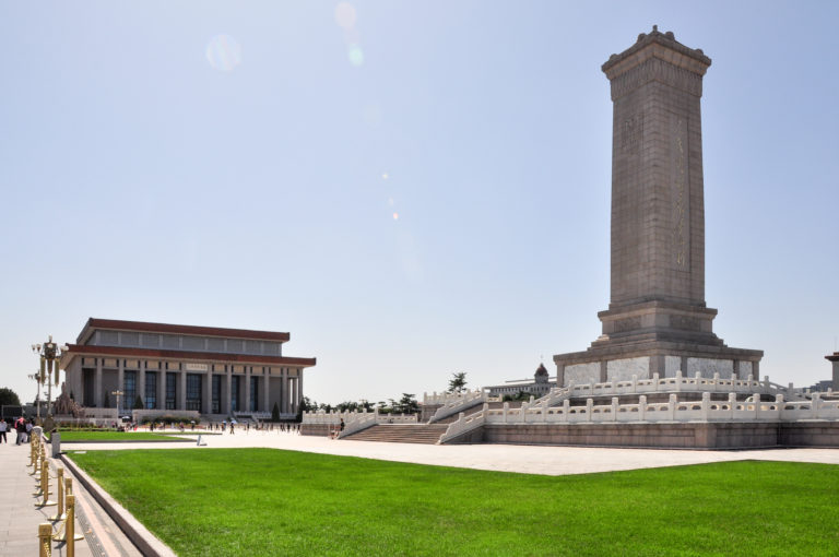 Stone obelisk of the Monument to the People’s Heroes on a balustraded platform, with the Great Hall of the People in the background.