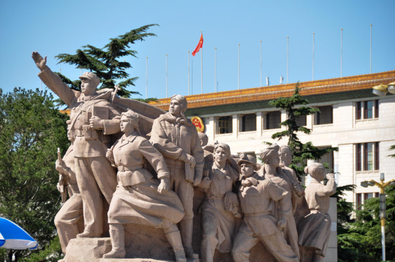 Monumental stone revolutionary sculptural group near the Monument to the People’s Heroes, showing workers, soldiers, and civilians in dynamic poses with a leading figure raising an arm.