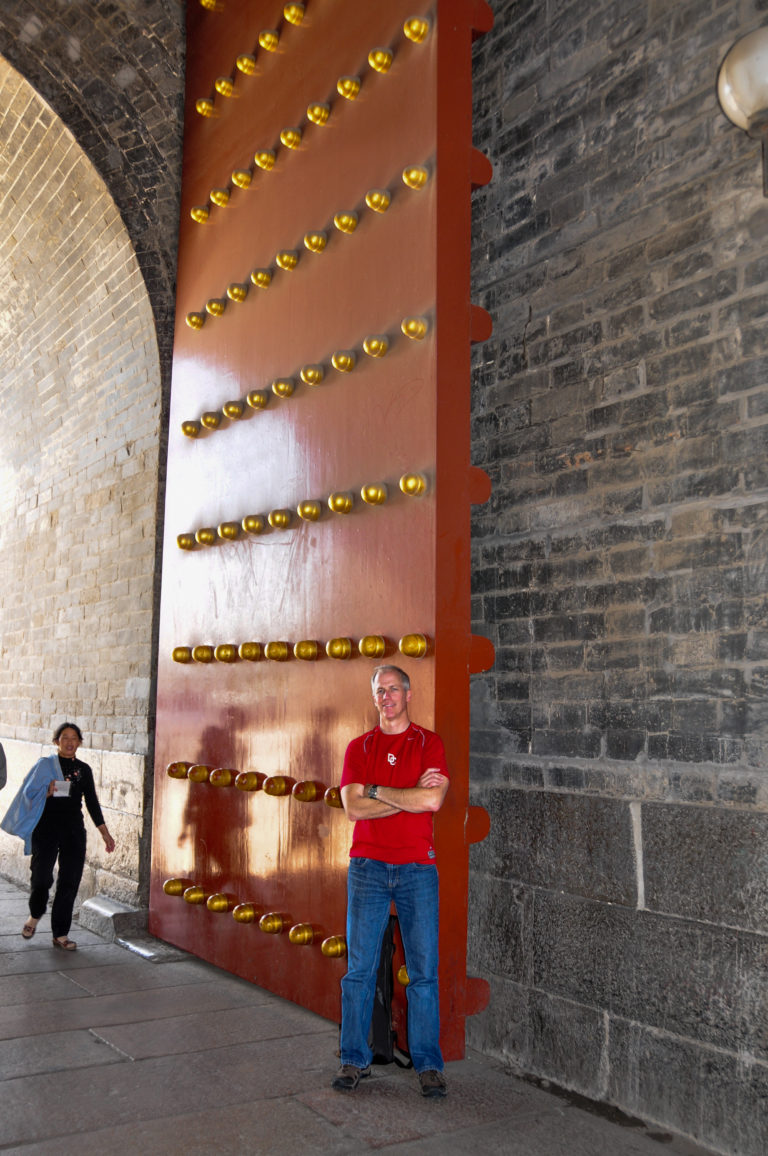 Visitor standing beside a massive studded red wooden gate inside the gray-brick passage of Zhengyangmen.