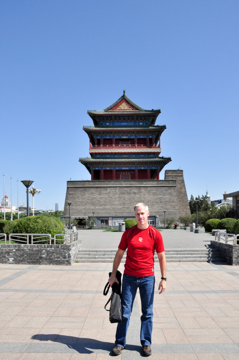 Male visitor in a red shirt standing in the paved plaza in front of Zhengyangmen Arrow Tower.