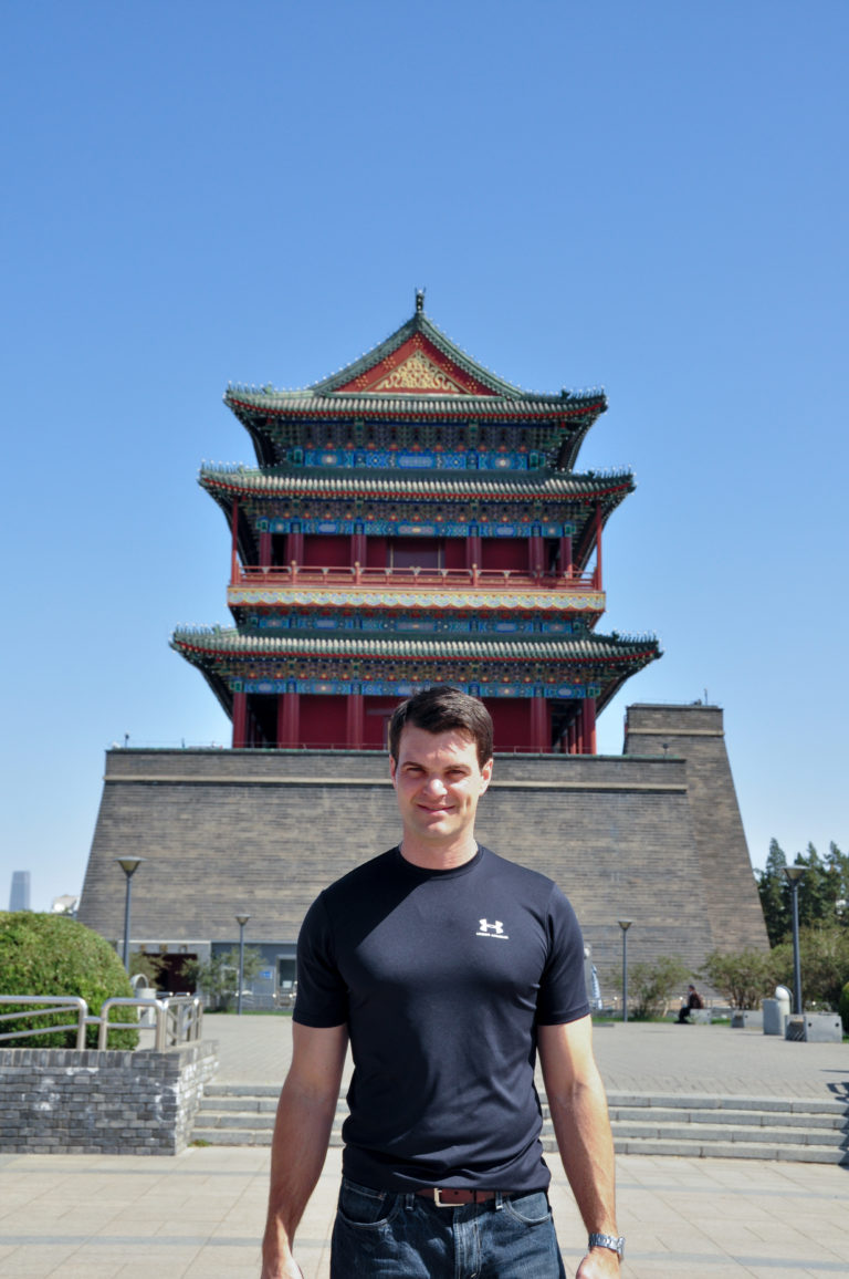 Man in a black shirt standing in front of Zhengyangmen Arrow Tower with its gray-brick base and tiered traditional roofs.