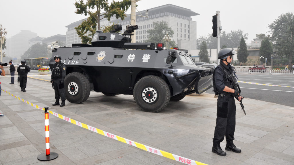 Armed police officers standing next to a black armored police vehicle behind tape in Tiananmen Square.