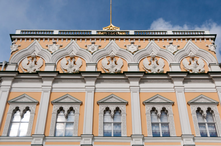 Upper ochre-and-white façade of the Grand Kremlin Palace with tall windows and repeated double-headed eagle reliefs.