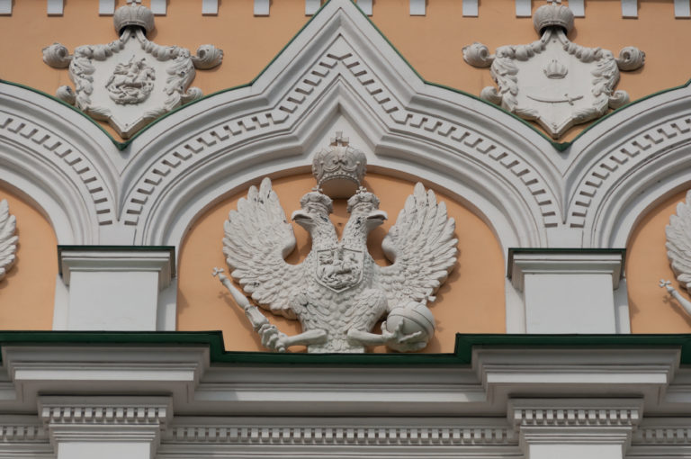 White double-headed eagle relief set within a pointed ornamental bay on the ochre Grand Kremlin Palace façade.