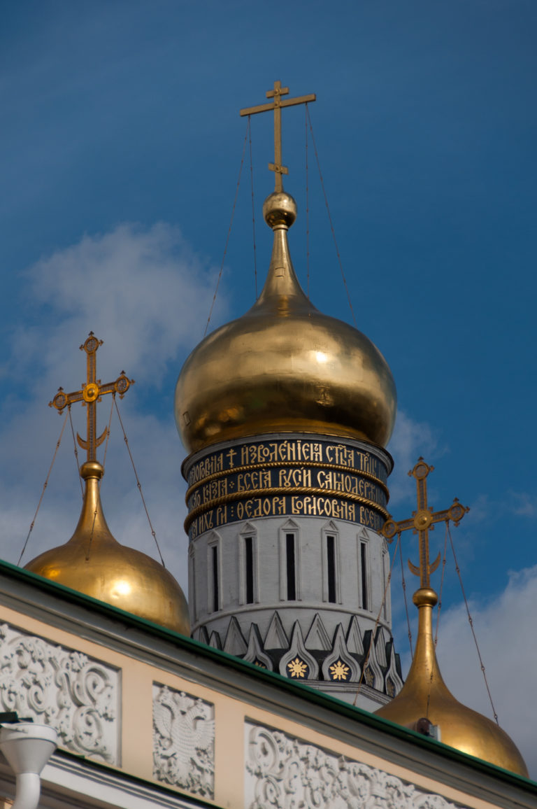 Close view of several gilded domes and crosses above the ornate white roofline of the Annunciation Cathedral.