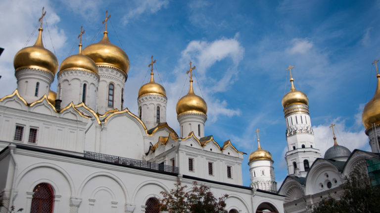 Clustered gilded domes of the Annunciation Cathedral with white walls and the Ivan the Great Bell Tower behind.