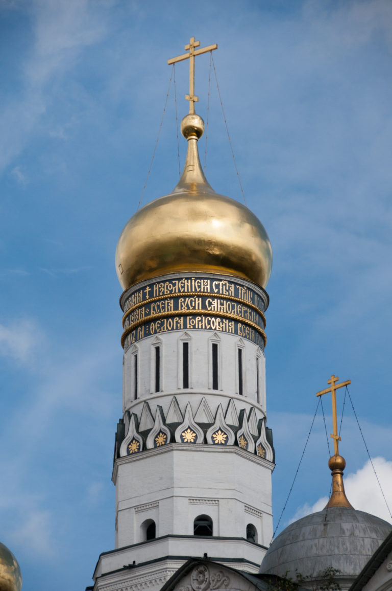 Gilded onion dome and white drum of the Annunciation Cathedral with inscription band and Orthodox cross.