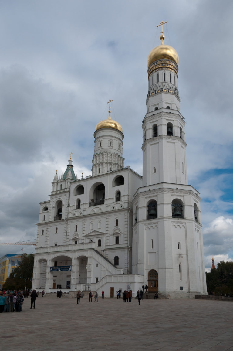 White Ivan the Great Bell Tower complex with arched belfries and gilded cupolas under a cloudy sky.