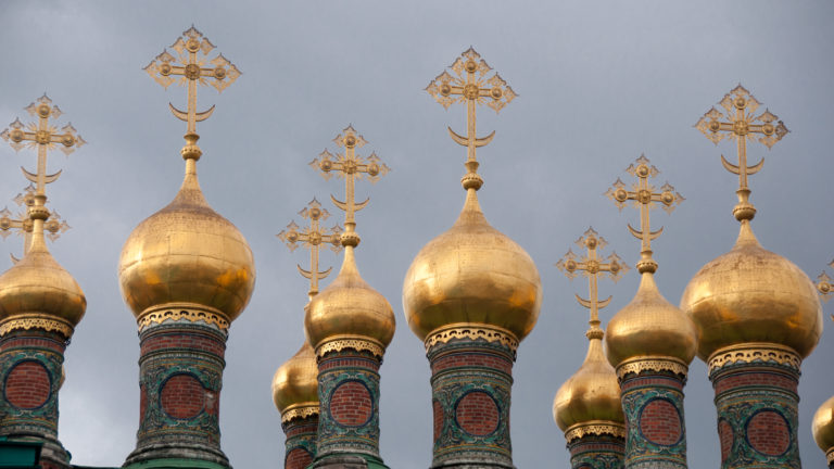 Gilded onion domes with intricate Orthodox crosses and patterned red-and-turquoise drums against a gray sky.