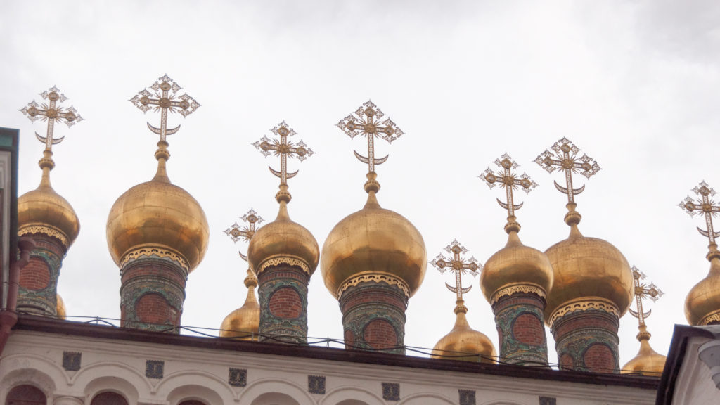 Cluster of gilded onion domes with ornate Orthodox crosses above richly patterned red-and-turquoise drums in the Kremlin.