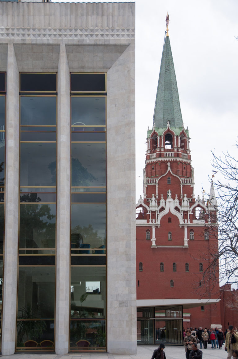 Red-brick Kremlin tower with green roof and star beside the pale stone-and-glass State Kremlin Palace.