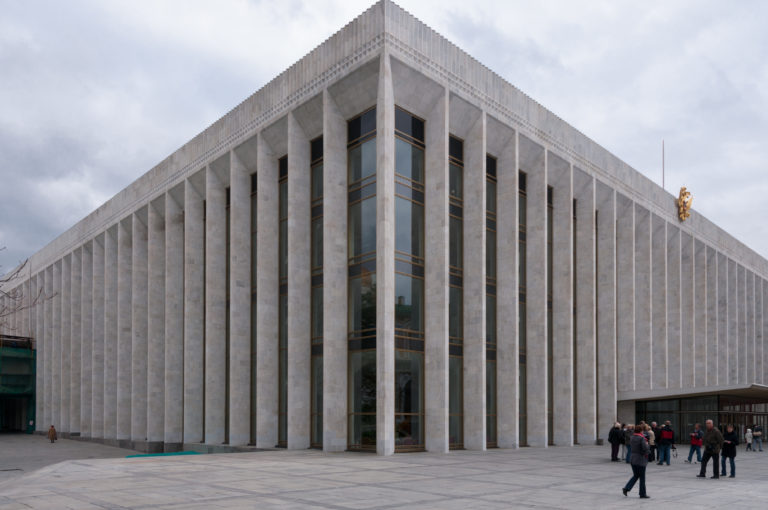 Modern State Kremlin Palace with tall pale stone fins, vertical glass bays, and visitors gathered near the entrance.