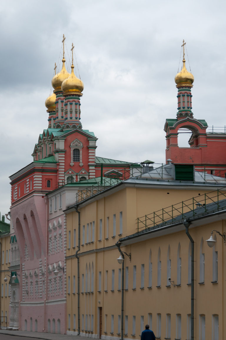 Gilded church domes and red-and-white decorative towers rising above a long yellow Kremlin building under a gray sky.