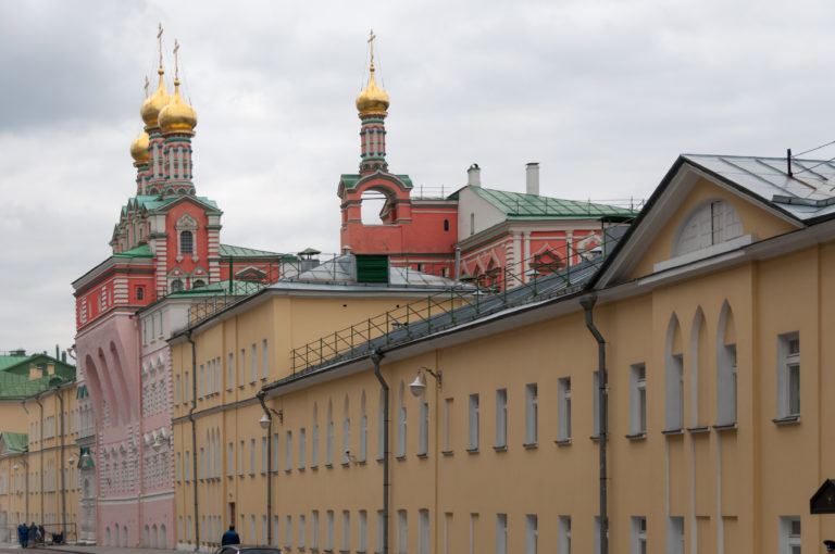 Red-and-white Orthodox church with gilded domes rising behind a long yellow building inside the Kremlin.