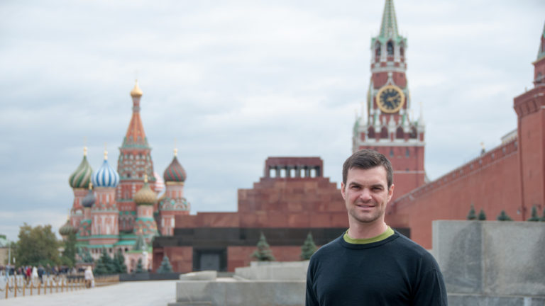 Visitor standing on Red Square with Saint Basil’s Cathedral, Lenin Mausoleum, and Spasskaya Tower softly focused behind.