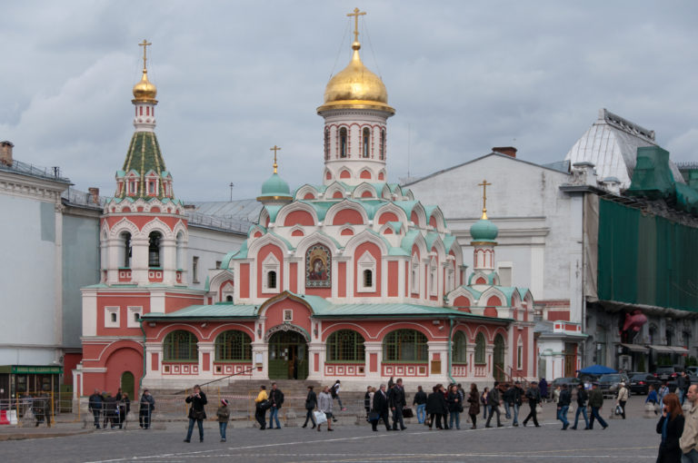 Red-and-white Kazan Cathedral with green roof accents and gilded domes, with visitors walking across the square in front.