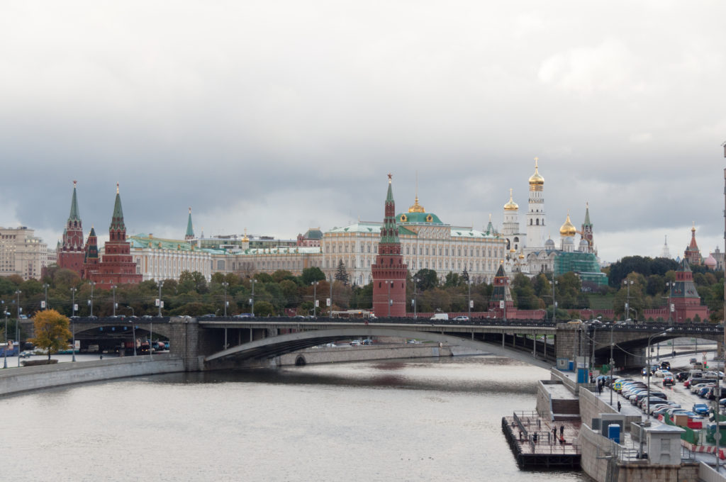 Wide view across the Moskva River toward the Kremlin, with a bridge, red towers, palace buildings, and golden domes.
