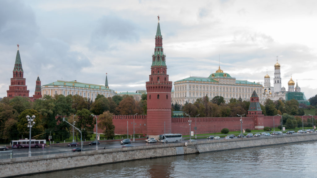 Kremlin walls and towers beside the Moskva River, with the Grand Kremlin Palace and gilded cathedral domes behind.