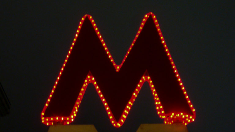 Red Moscow Metro M sign outlined by small yellow-orange lights against a dark night sky.