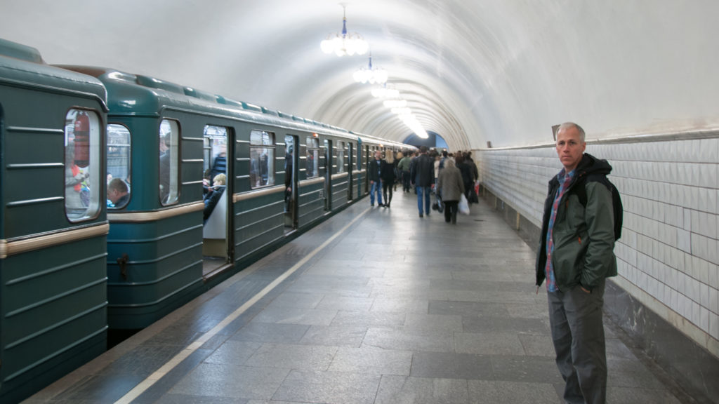 Dark green metro train along a white-vaulted platform with passengers walking into the distance and a man in foreground.