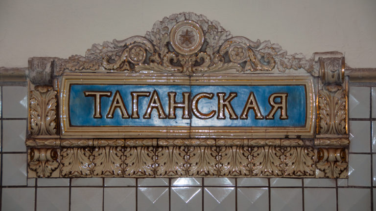 Cyrillic ТАГАНСКАЯ station name on a turquoise panel framed by ornate cream and gold floral molding.