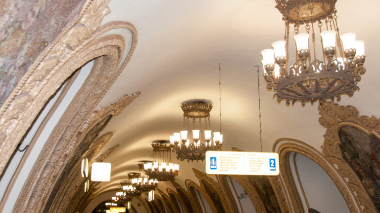 Ornate chandeliers receding beneath a white metro vault beside richly framed arched wall panels.